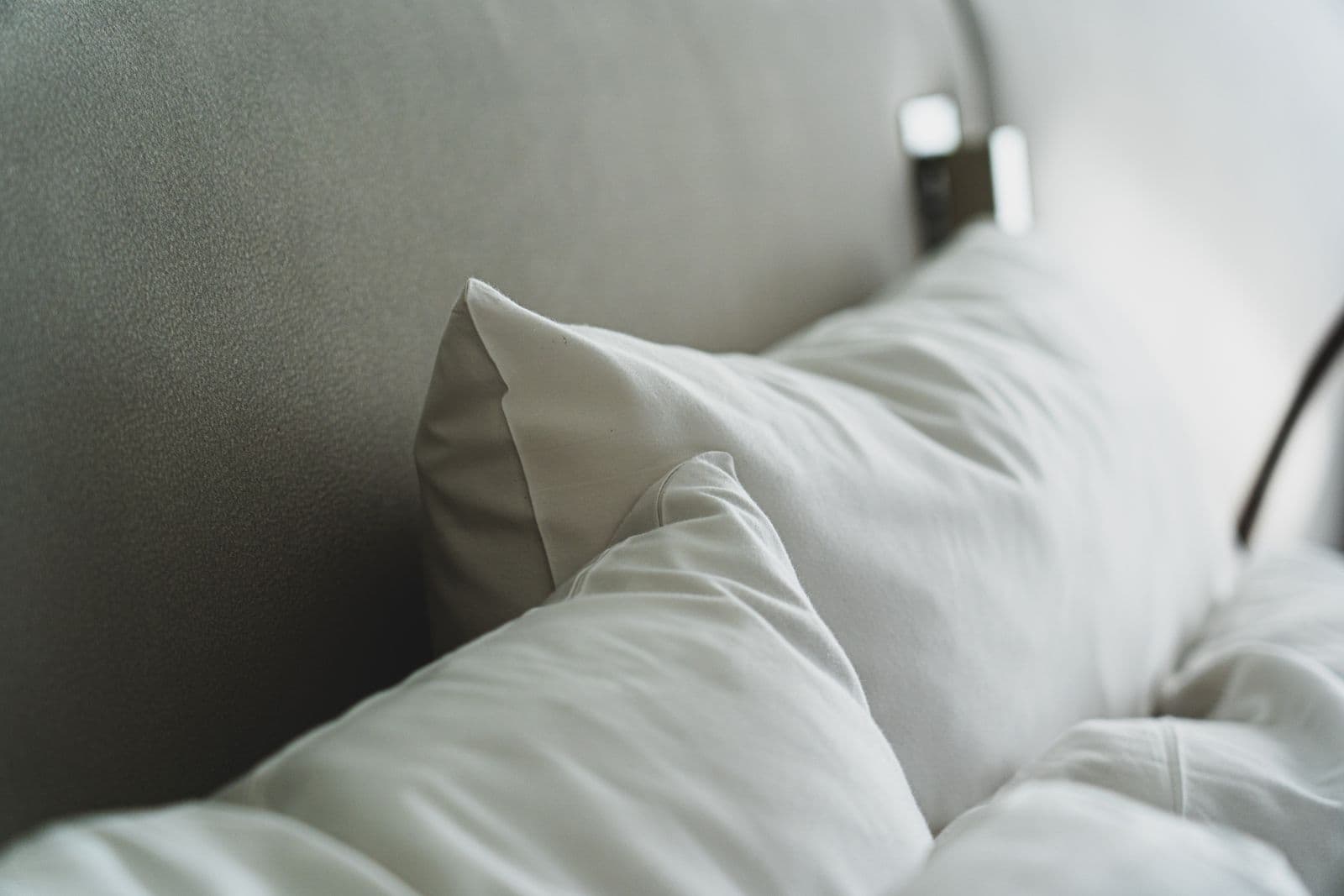White pillows propped against an upholstered headboard on a made bed