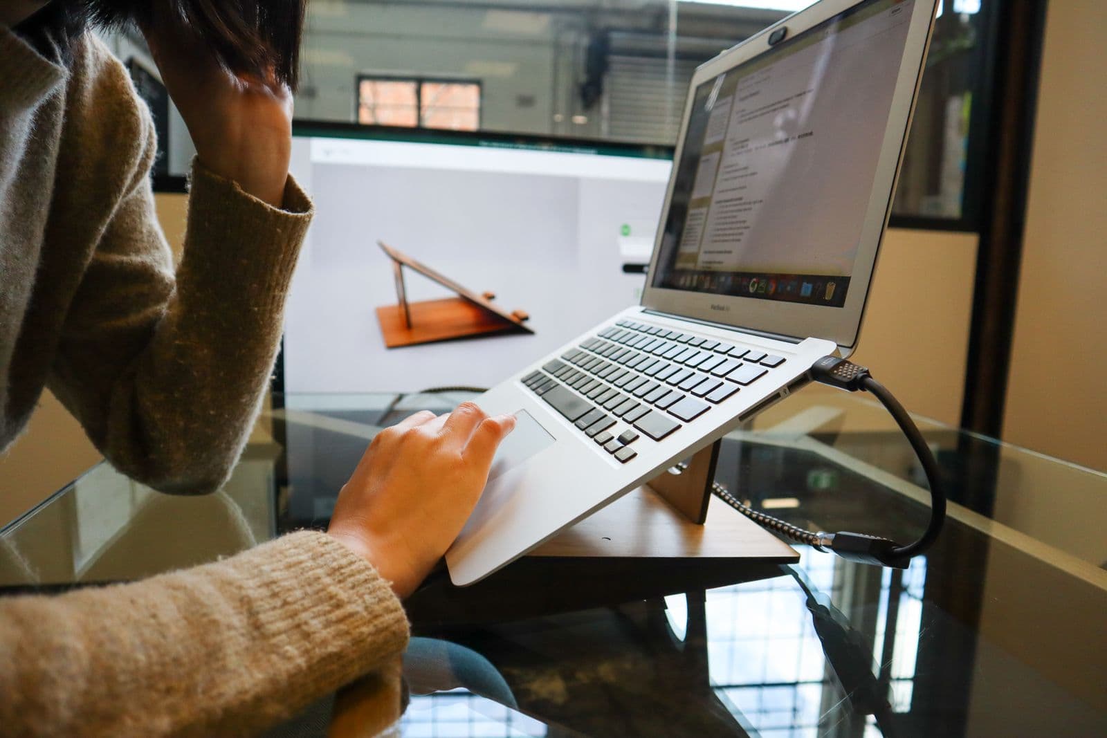 A woman working at a laptop raised on a stand at a desk
