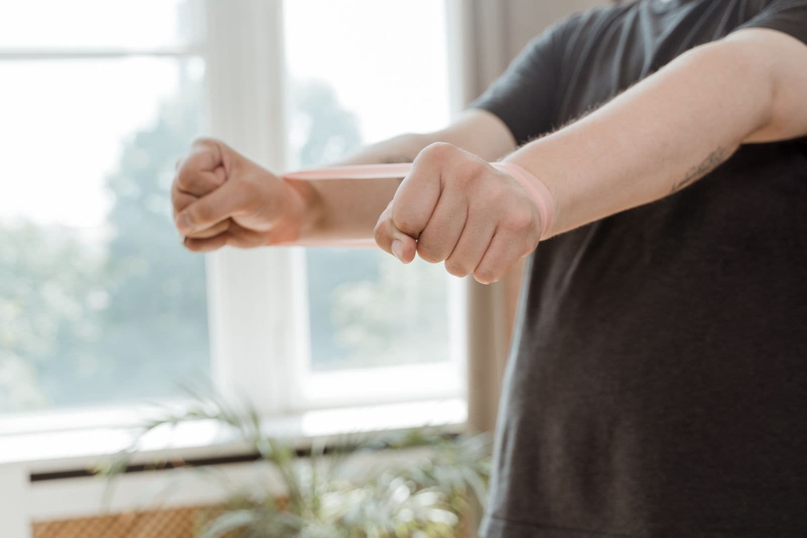 A person in a gray shirt using a resistance band for an arm exercise indoors