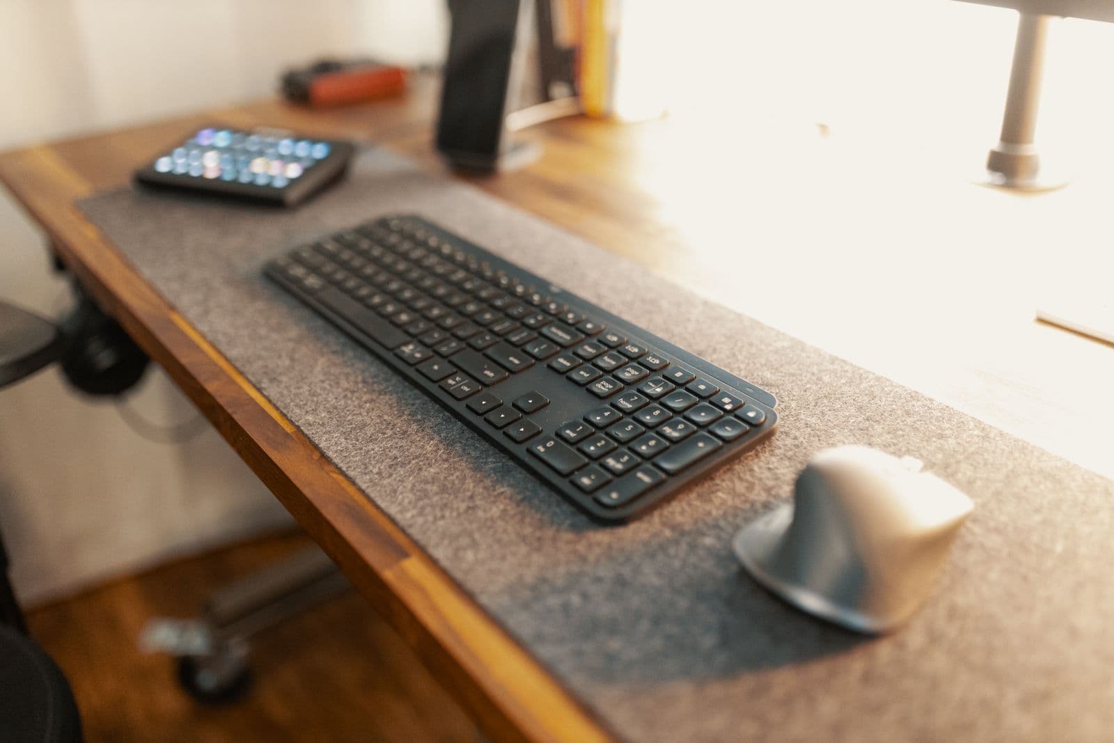 A keyboard and ergonomic mouse on a wooden desk in natural light