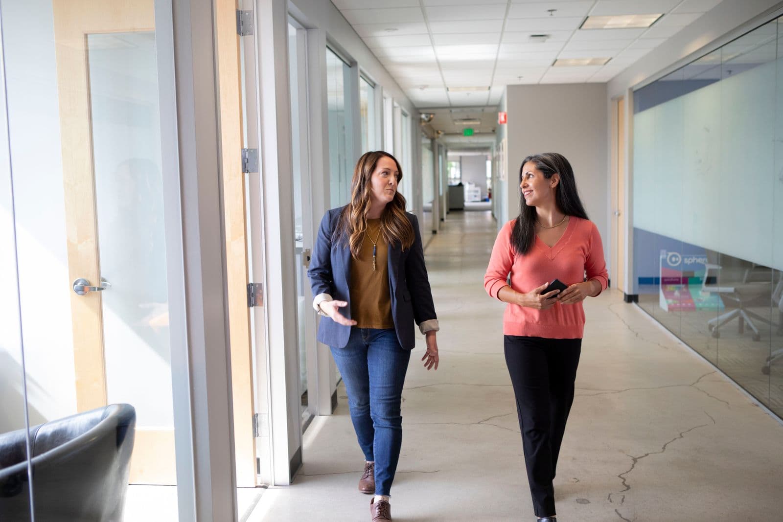 Two colleagues walking and talking along an office corridor