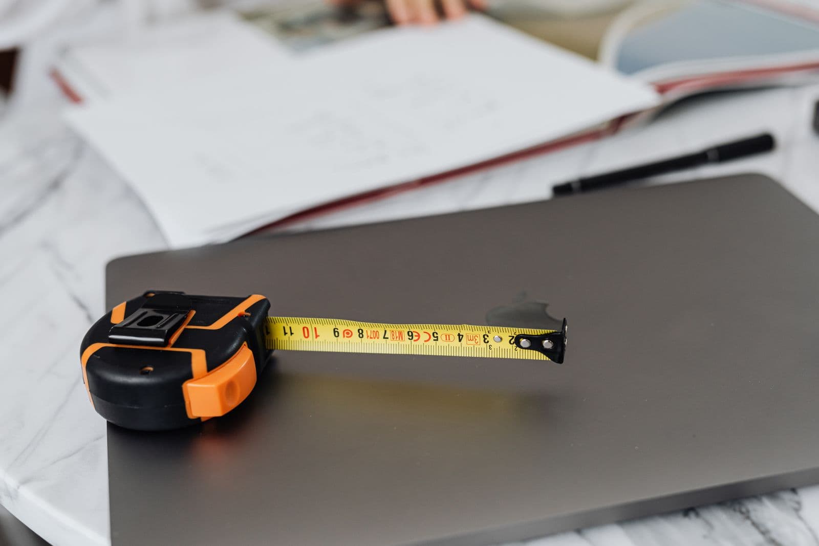 A retractable tape measure resting on a desk beside a laptop