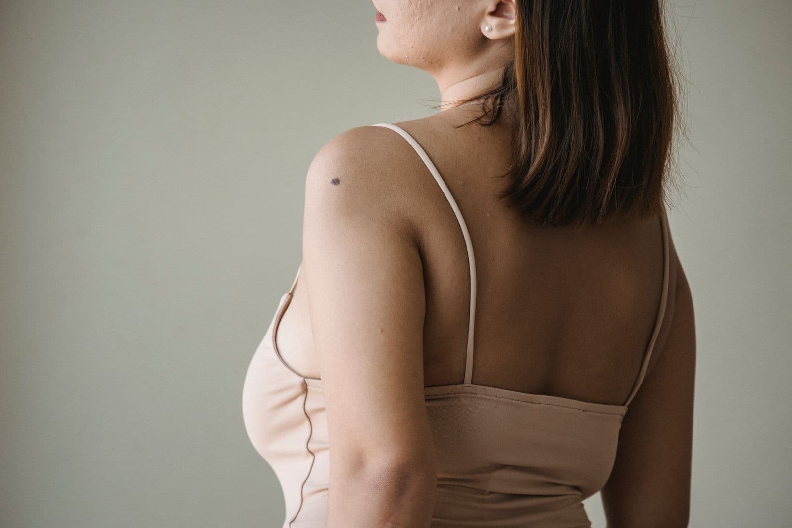 A woman seen from behind in a fitted beige top, showing her shoulders and upper back
