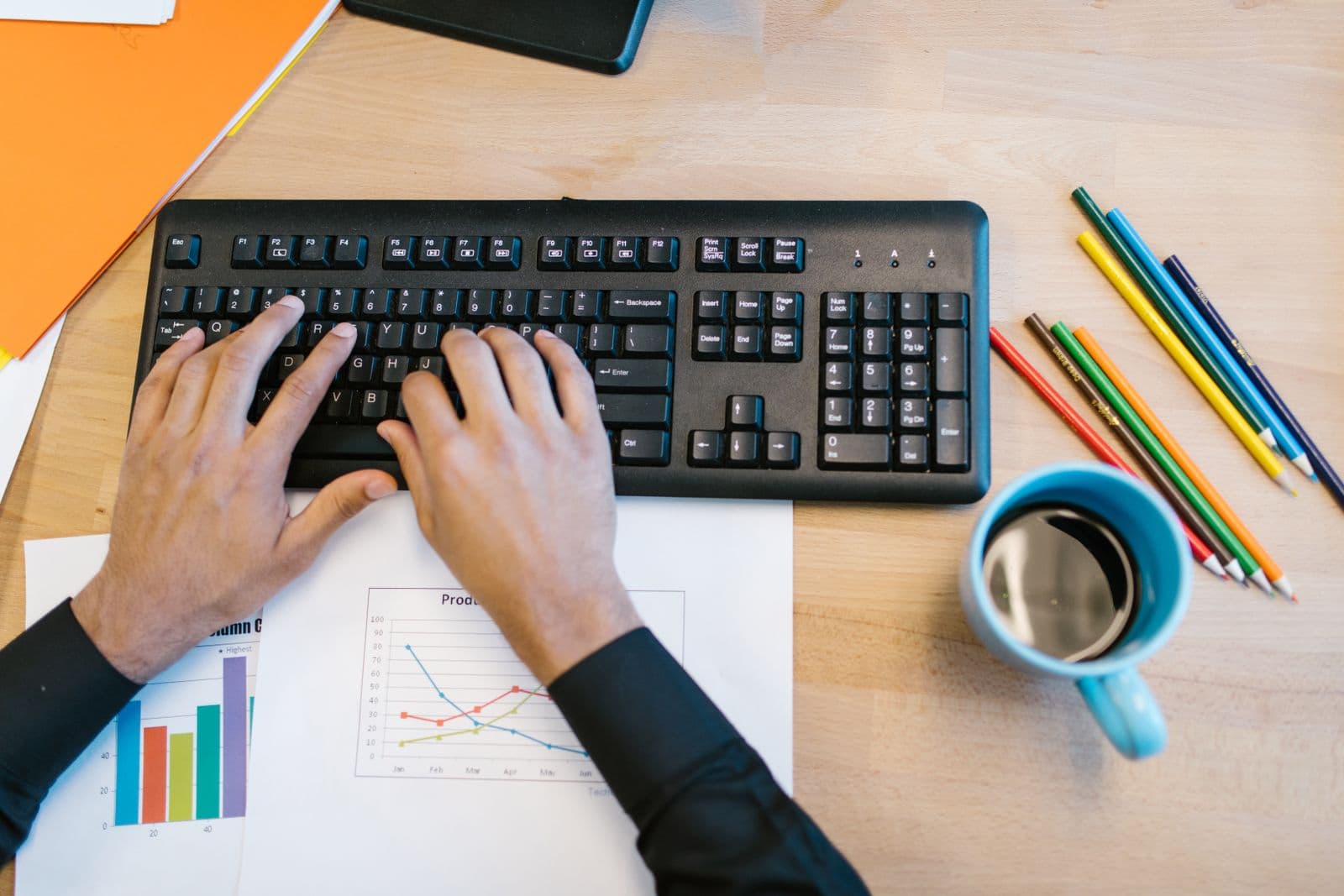Hands typing on a keyboard with printed charts lying flat on the desk in front of it