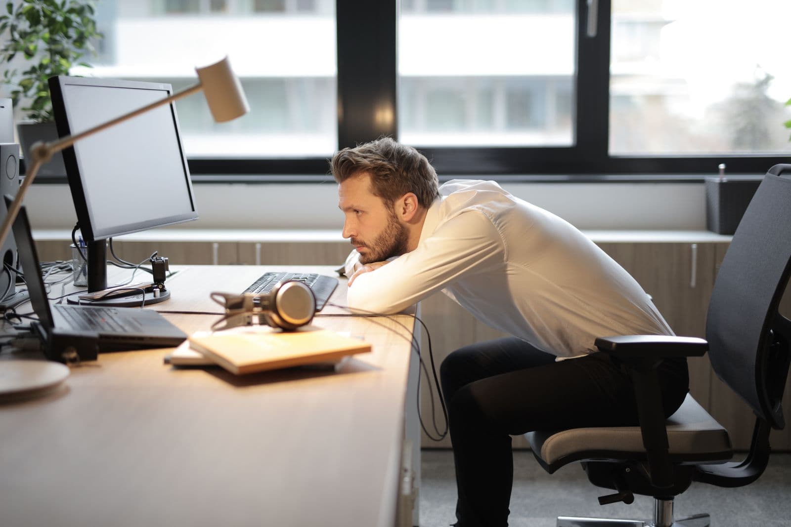 A man slumped over his desk, leaning close to his computer screen