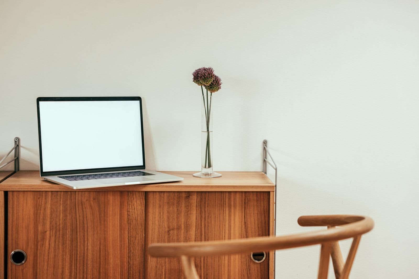 A laptop open on a shallow wooden cabinet against a plain wall