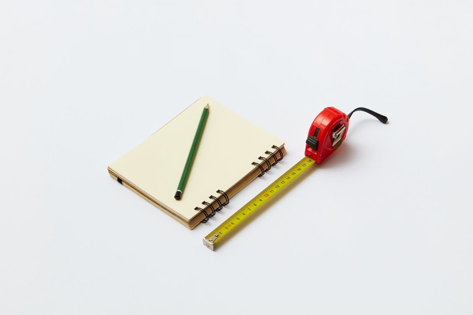 A notebook, pencil and retractable tape measure on a plain surface