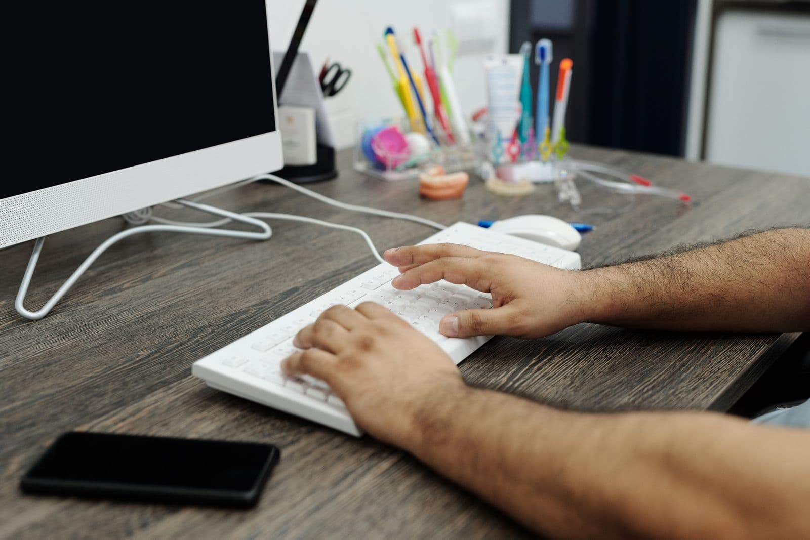 Hands typing on a white keyboard at a wooden desk