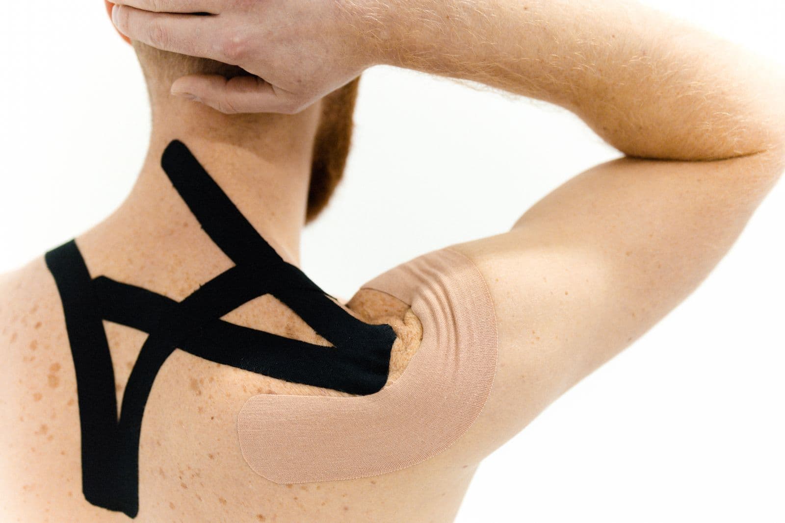 A man seen from behind with kinesiology tape applied across his upper back and shoulder