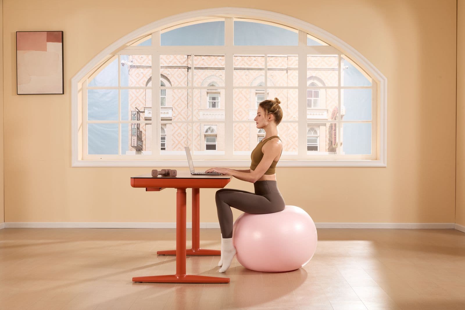 A woman working on a laptop while sitting on an exercise ball at a desk