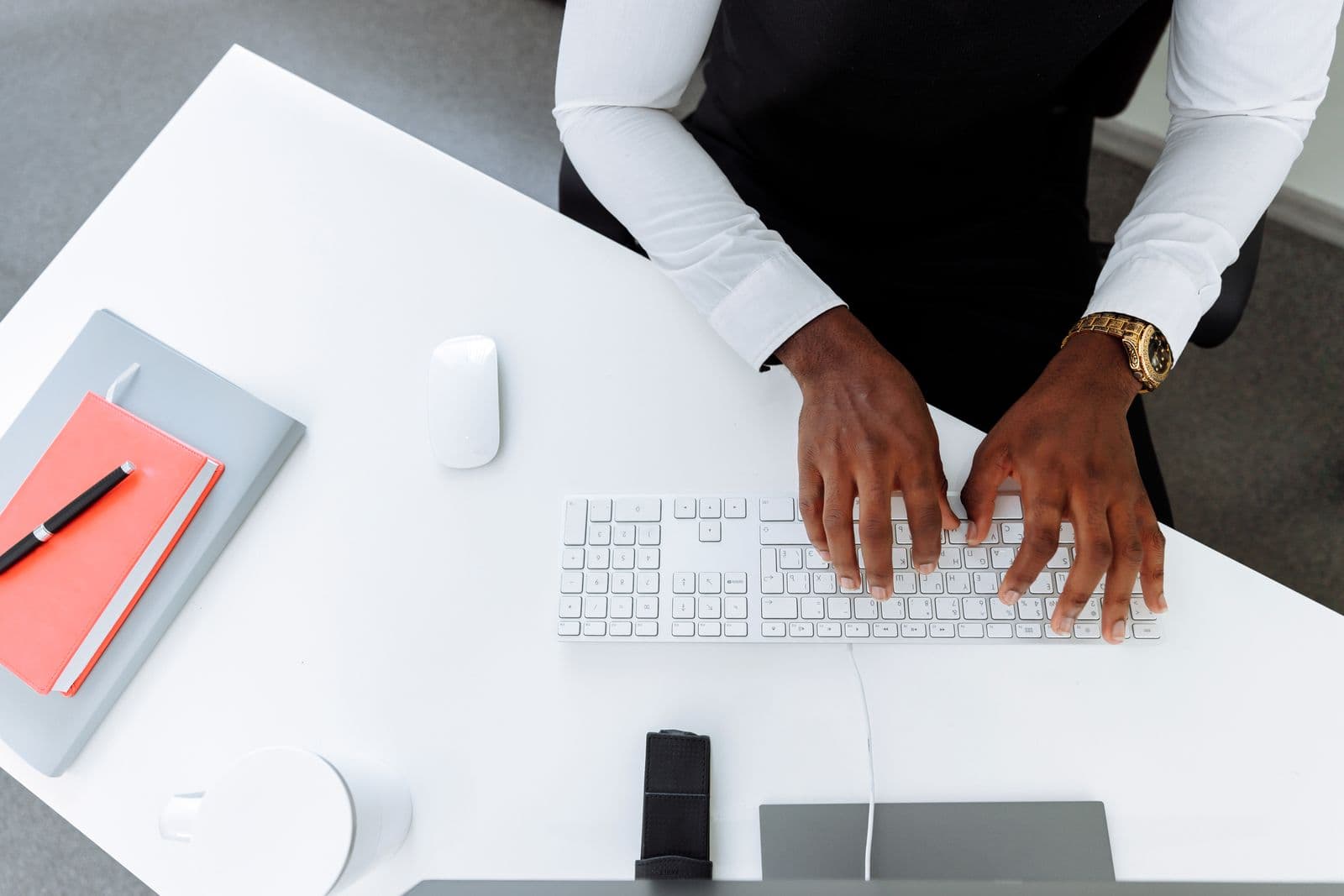 A person typing at a keyboard on a desk, forearms and hands visible