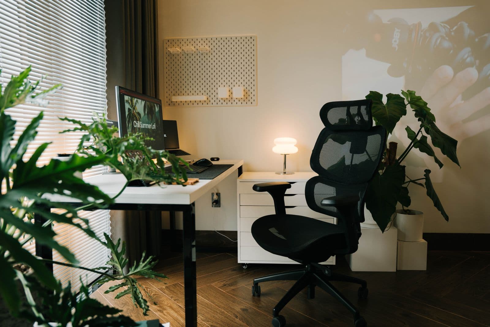 A black mesh office chair with a headrest at a white desk in a home office with plants