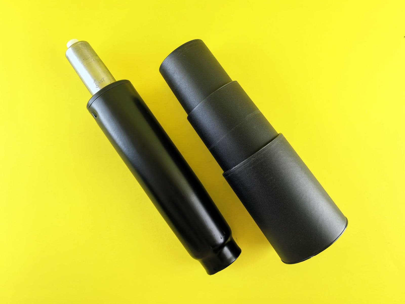 Two black gas lift cylinders for office chairs on a bright yellow background