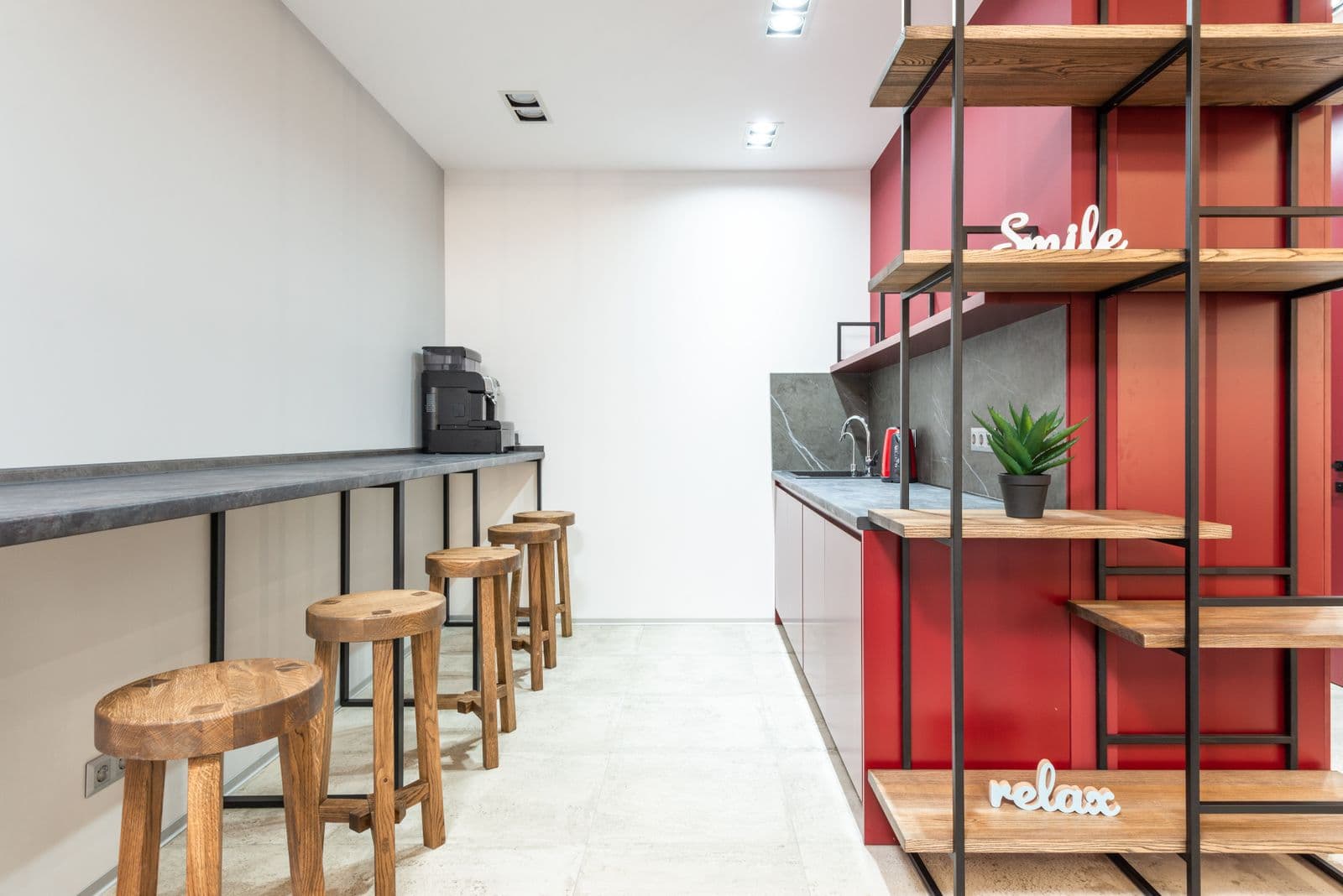A row of tall wooden stools pulled up to a long counter-height bench in a bright office kitchen