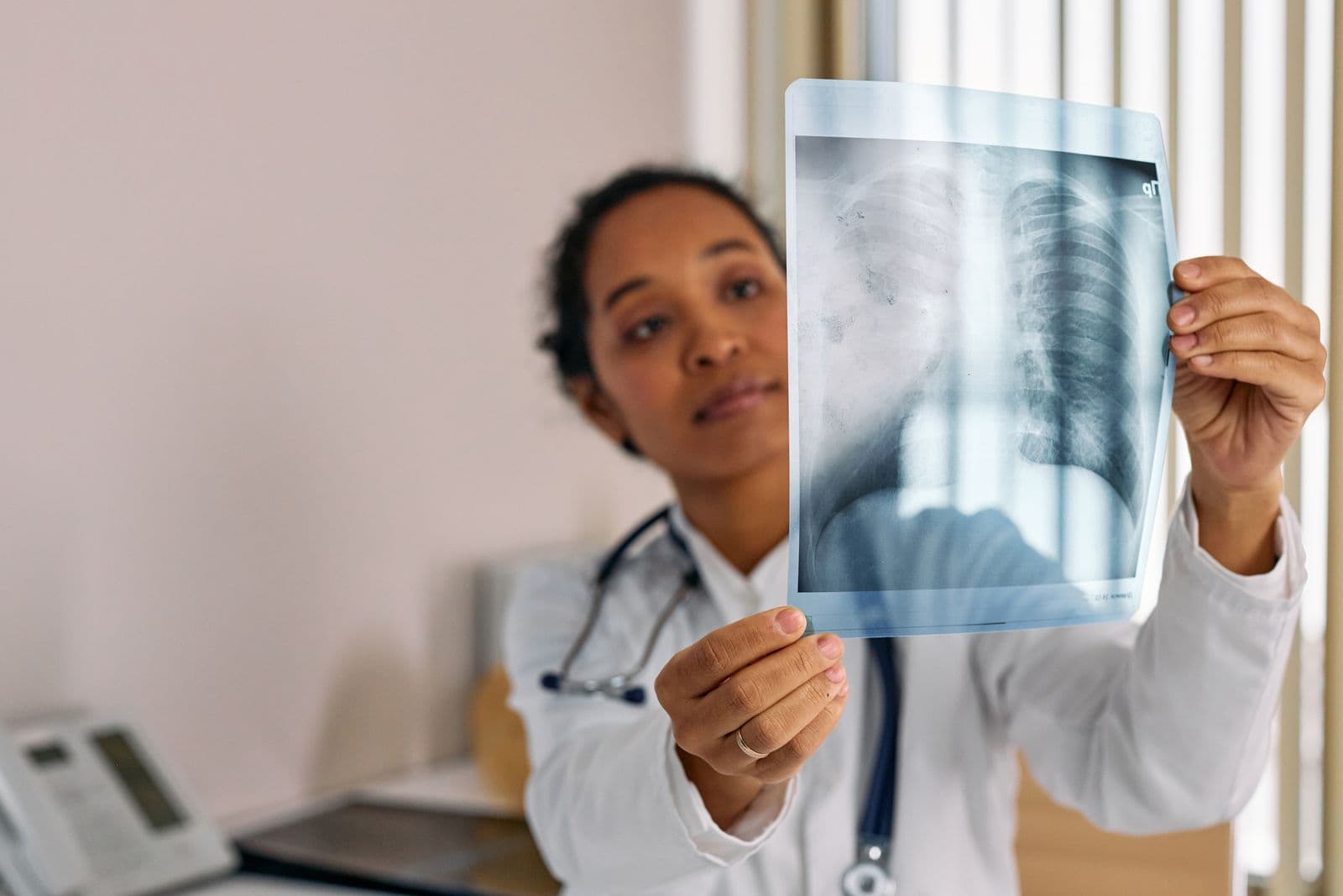 A doctor in a white coat holding a chest X-ray film up to the light in a clinic office