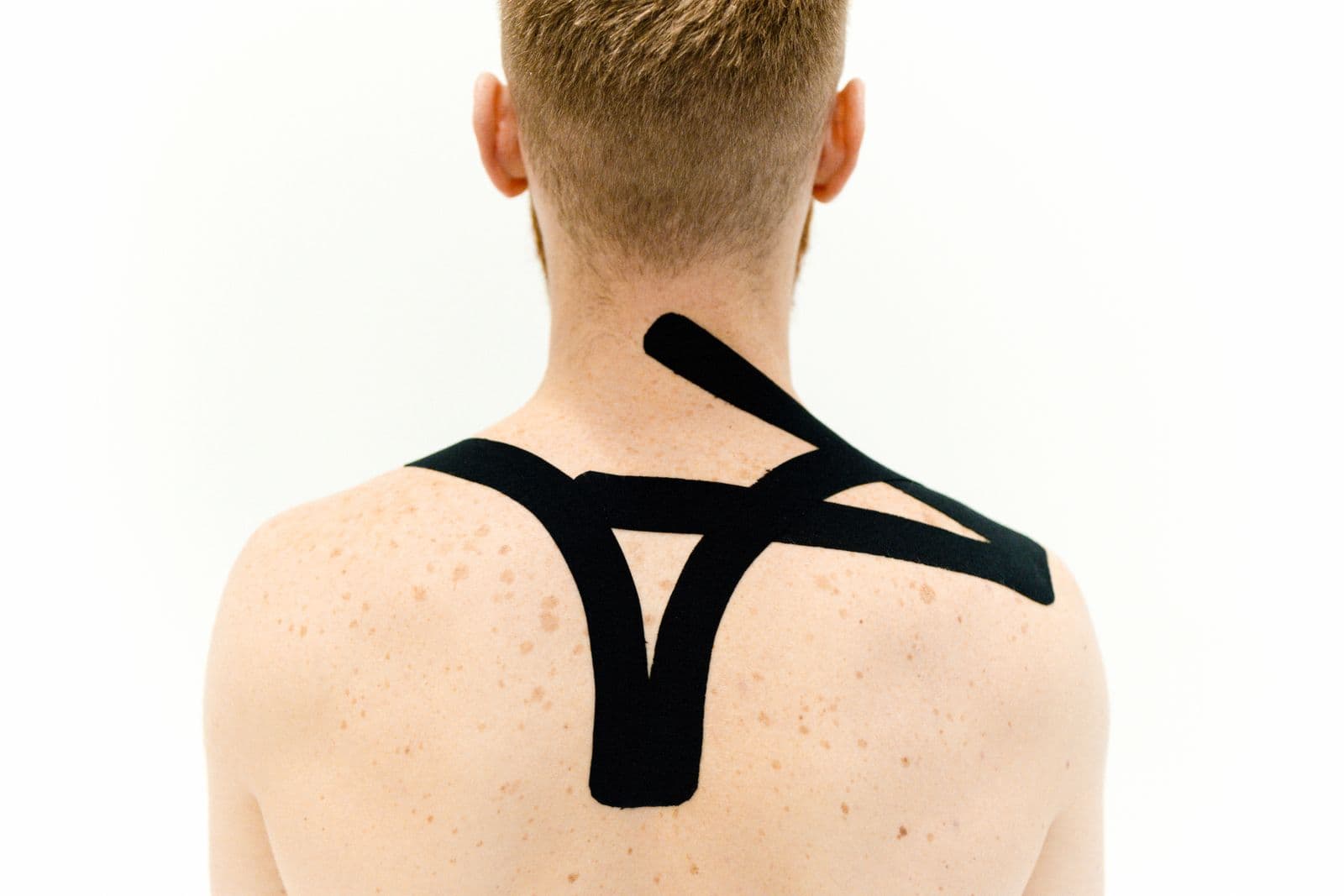Kinesiology tape applied across a person's upper back and shoulders