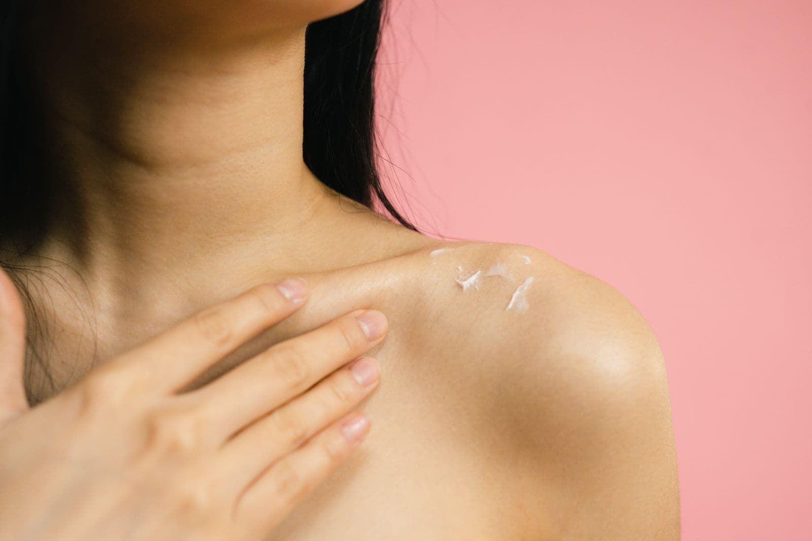 A woman applies moisturizing cream to her shoulder