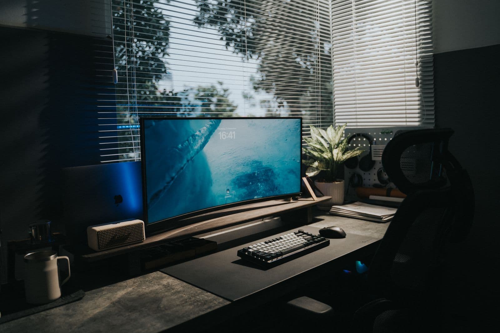A home office with a curved monitor on a desk beside a window
