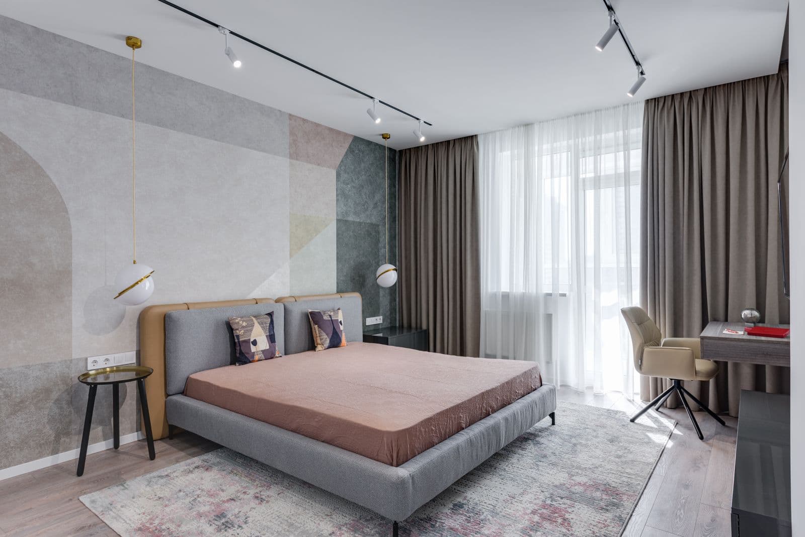 A bedroom with a narrow desk and an armchair fitted beside a curtained window