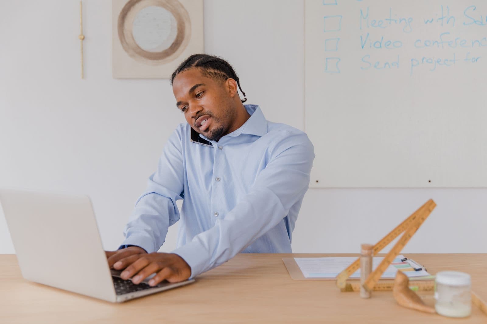 A man at a desk typing on a laptop with a phone pinned between his ear and raised shoulder