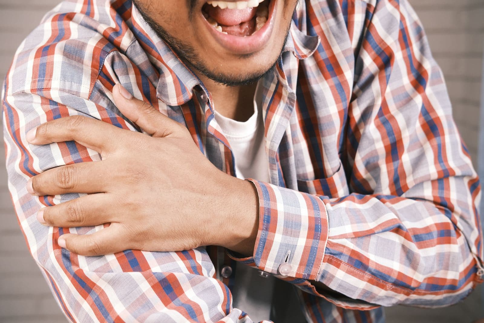 A man in a plaid shirt gripping the front of his shoulder with one hand